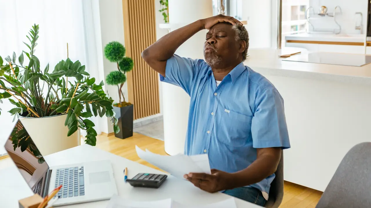 mature senior man holds head frustrated overwhelmed paperwork