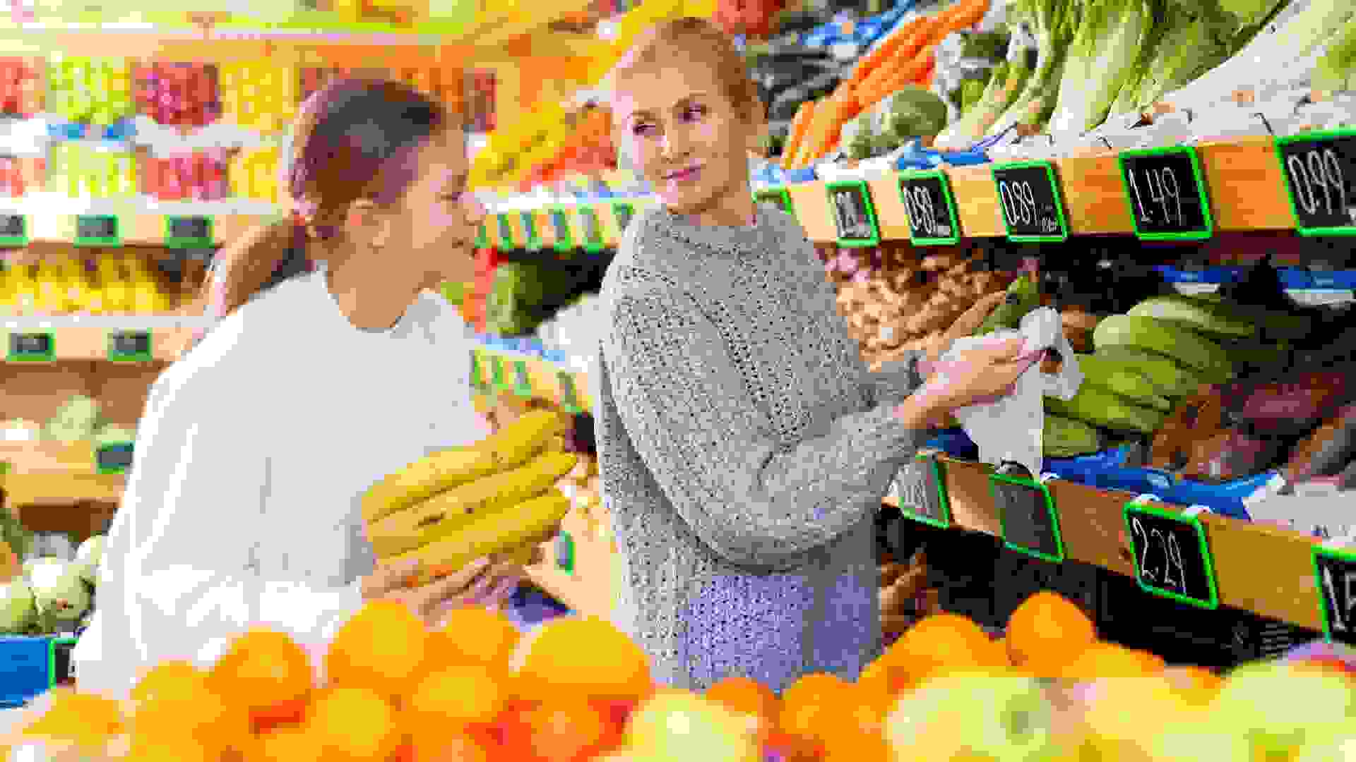 Smiling teenage girl with mother choosing fruits and vegetables in supermarket stock photo