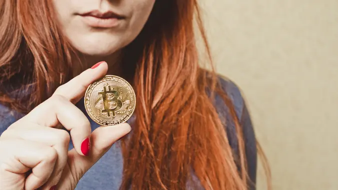 Red-haired woman holds bitcoin gold coin in her hand stock photo