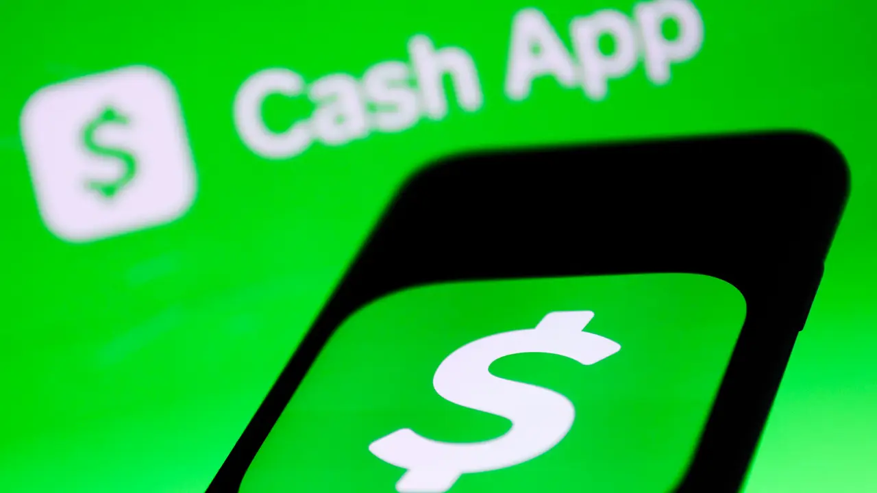 Cash app icon displayed on a phone screen and cash app logo displayed on a laptop screen are seen in this photo