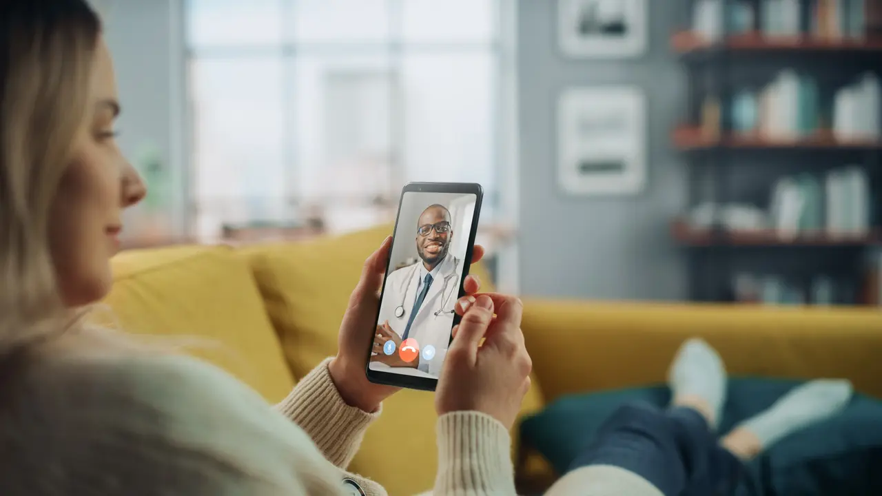 Close Up of a Female Chatting in a Video Call with Her Black Male Family Doctor on Smartphone from Living Room.