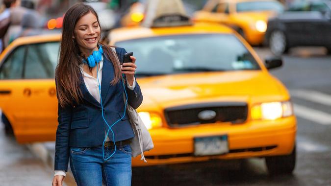 Young woman walking in New York city using phone app for taxi ride hailing with headphones commuting from work. Asian girl happy texting on smartphone. Urban walk commuter NYC stock photo