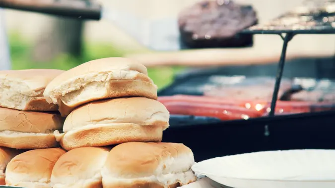 a cookout of hamburgers and hot dogs with buns in the foreground.