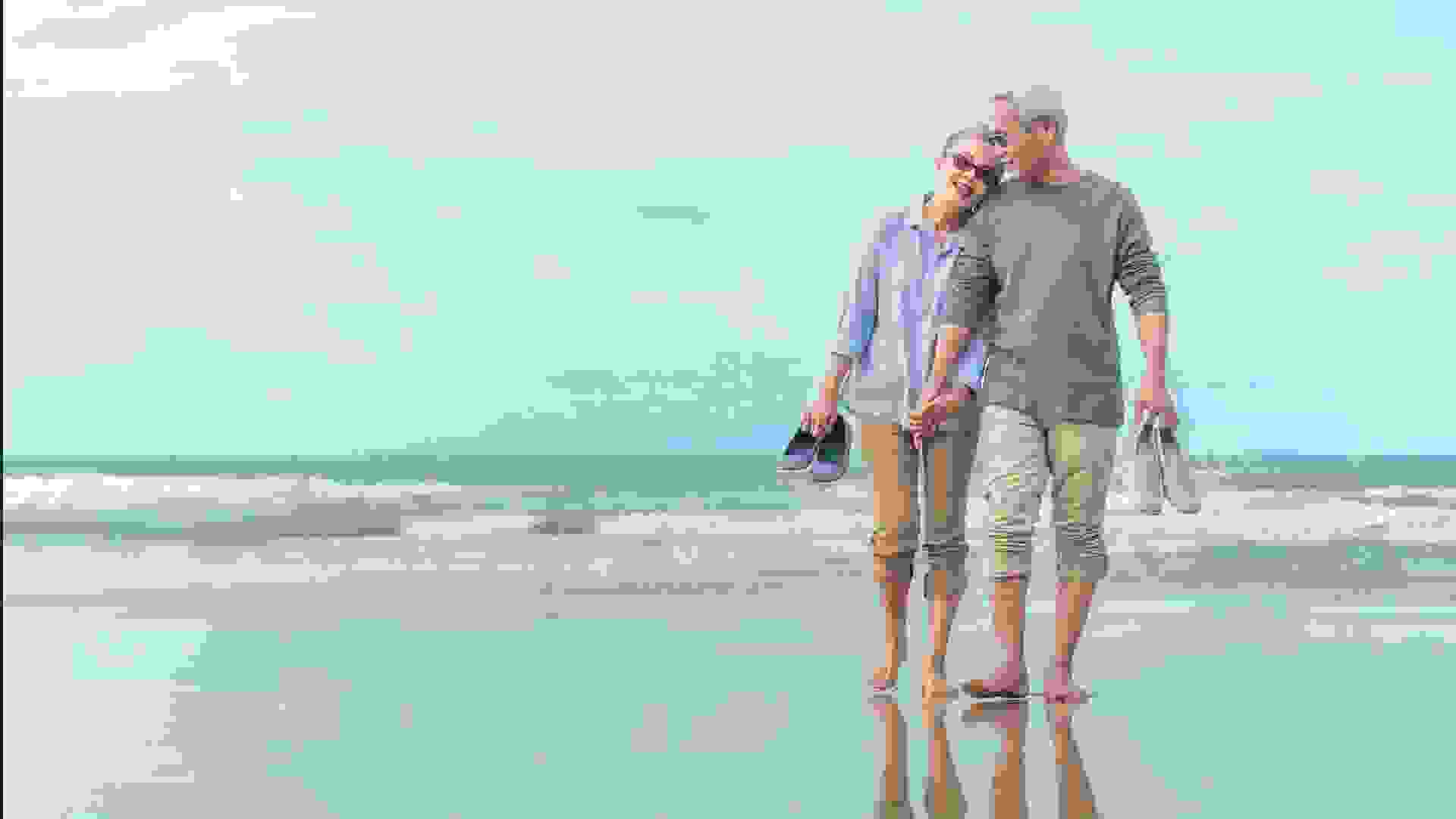 Age, Travel, Tourism and people concept - happy senior couple holding hands and walking on summer beach.