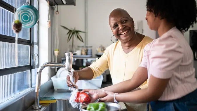 Grandmother and granddaughter washing vegetables together at home stock photo