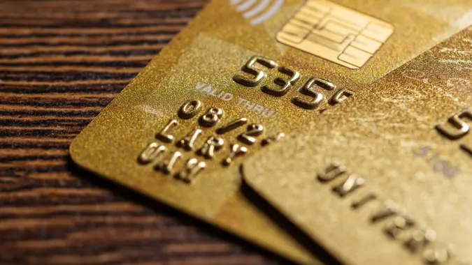 Stock photo of the corner of two golden credit cards sitting on top of each other on a wood table.