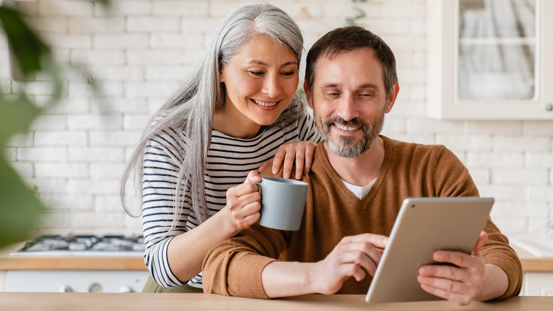 Happy mature middle-aged family couple parents husband and wife checking emails, reading news on digital tablet during breakfast, choosing new house, using application online stock photo