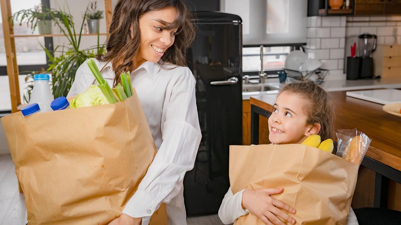 Cheerful little daughter helping the mother to carry groceries from the market stock photo