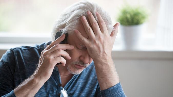Frustrated elderly mature retired man feeling upset desperately talking on the phone with debt problems, stressed sad middle aged man depressed by hearing bad news during mobile conversation at home.