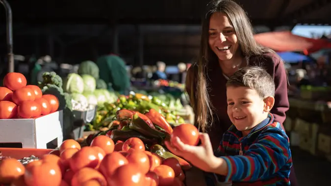 A cute boy is picking out vegetables with his mom at the farmers' market.