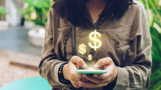 Une femme utilise un smartphone mobile gadget pour gagner de l'argent en ligne avec l'icône dollar pop-up.