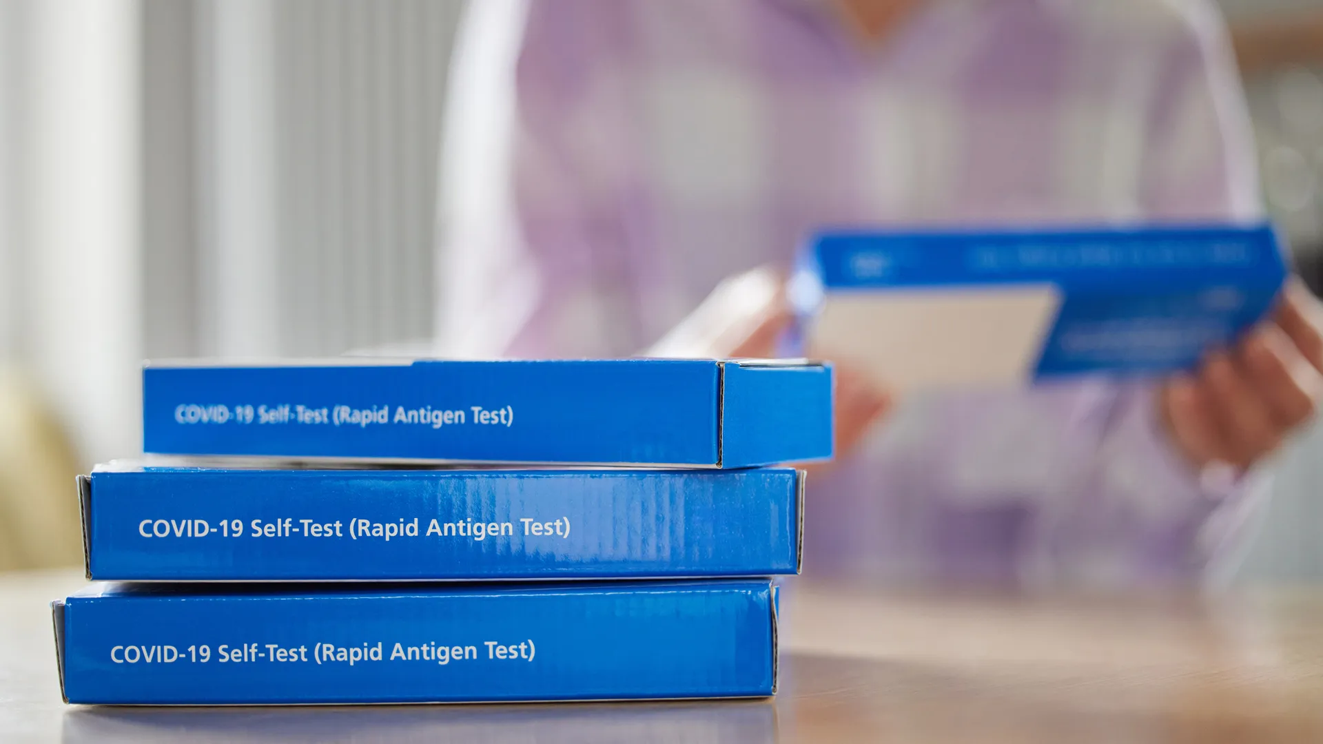 Close Up Of Woman At Home Reading Instructions On Supply Of Covid-19 Rapid Antigen Self-Testing Kits.