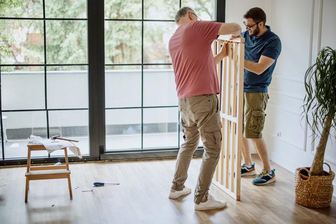 Senior father and mid adult son, installing bed frame together on father’s day.