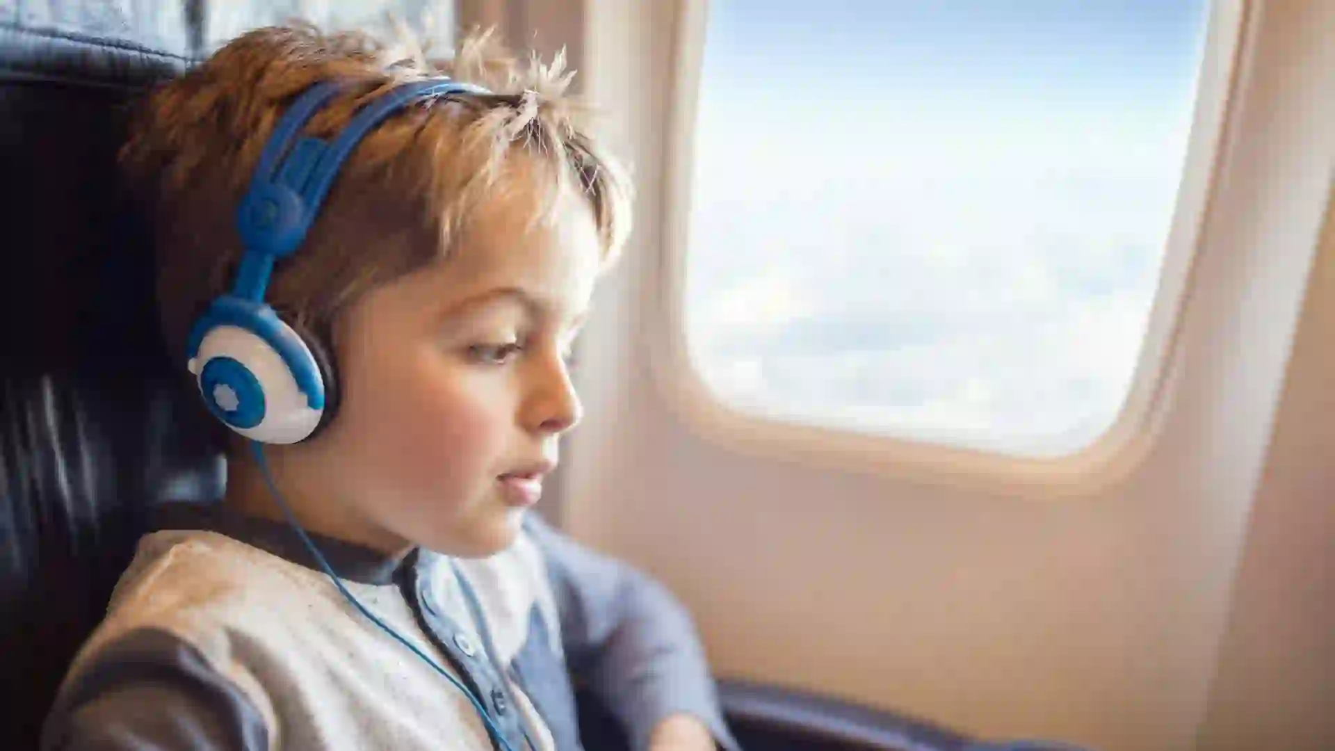 Boy with headphones watching and listening to in flight entertainment on board airplane.