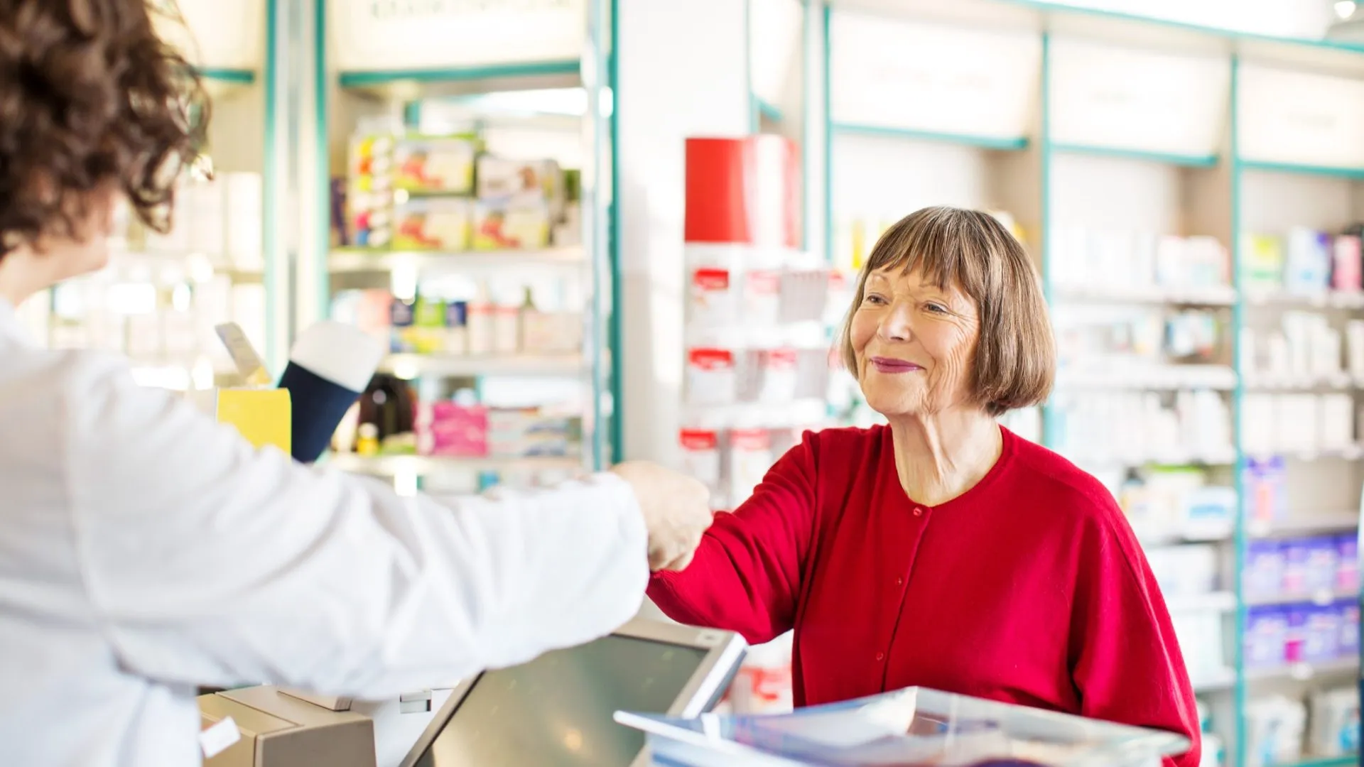 Senior female customer standing at chemist counter as pharmacist hands her medication order.