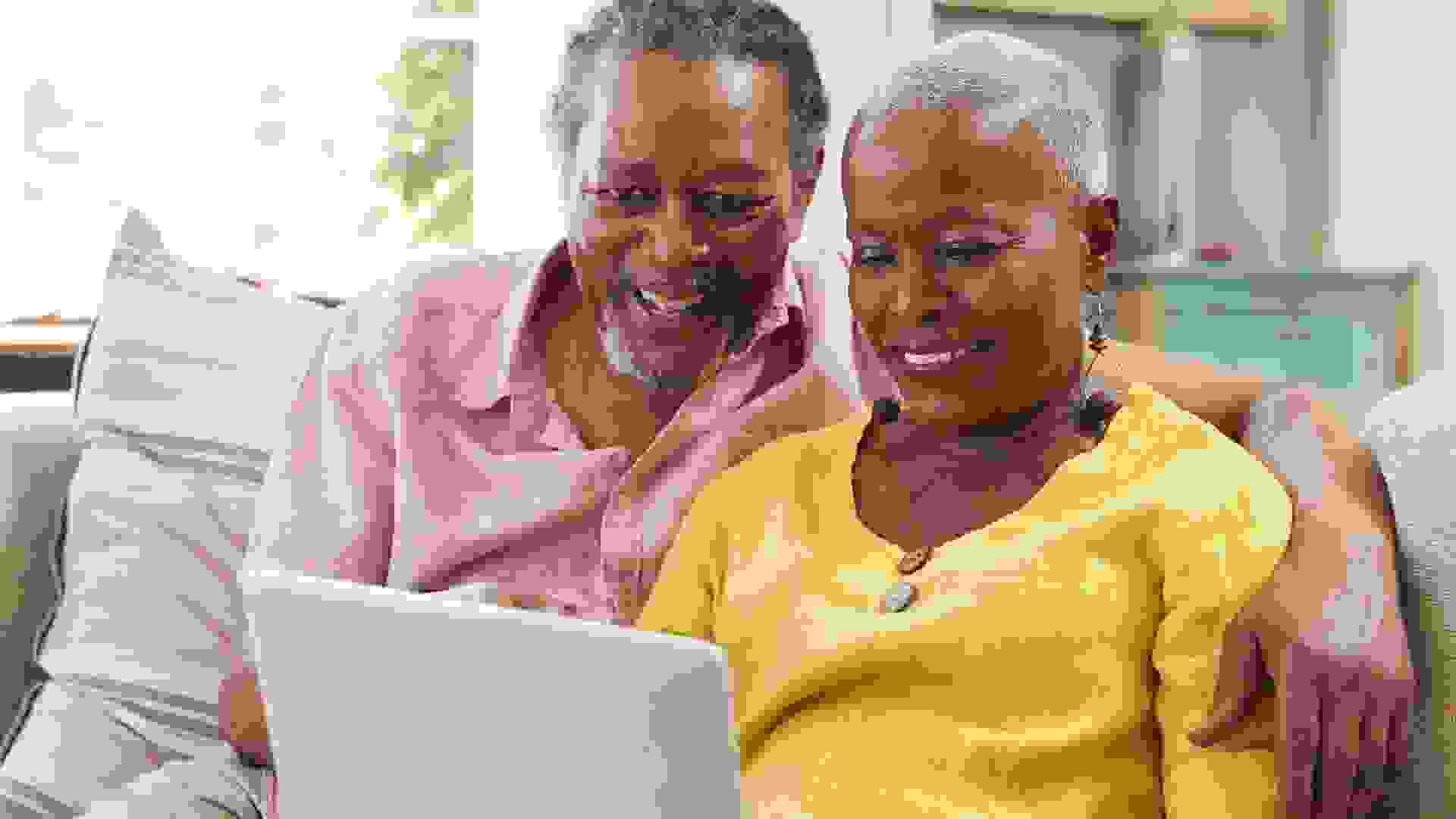 Senior Couple Sitting On Sofa Using Laptop At Home Together stock photo