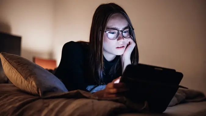 Angry looking Teenage Woman relaxing on Bed at Night using her Digital Tablet stock photo