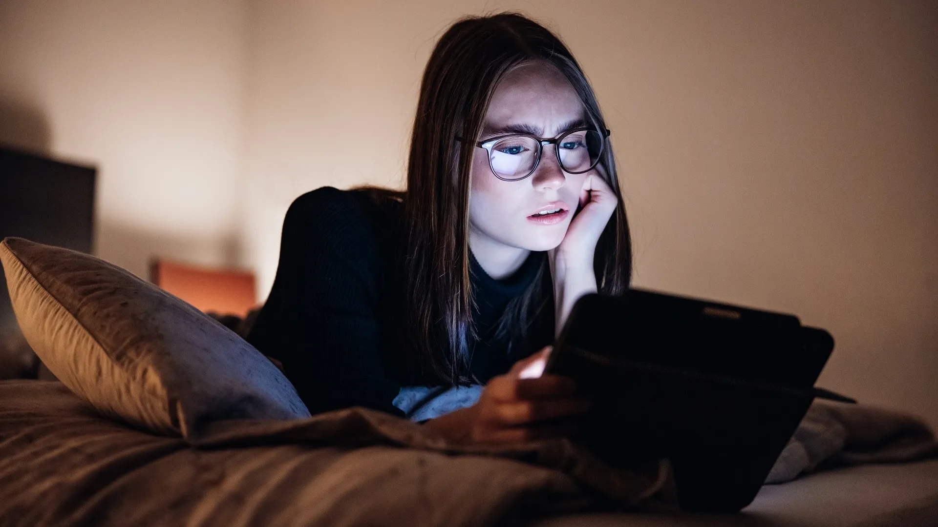 愤怒的少女在床上放松在晚上使用她的数字平板电脑的股票照片