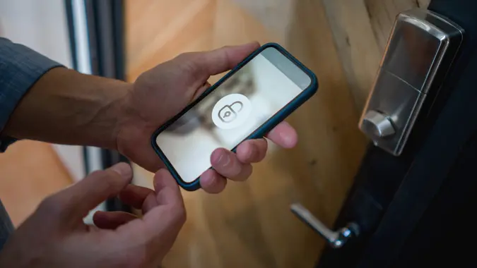 Close-up on a man opening the door of his house using a home automation system on his cell phone - smart homes concepts.
