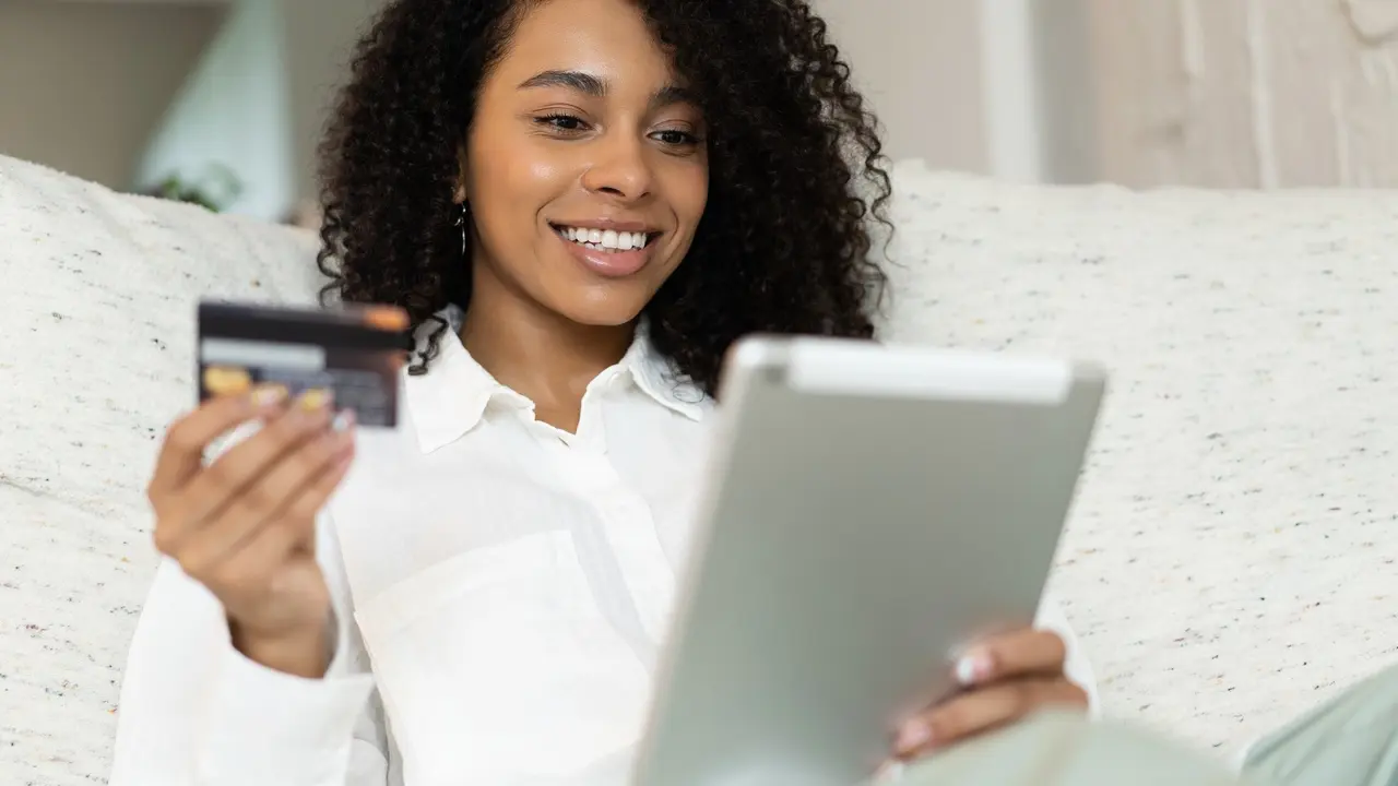 Young african american woman holding credit card and using tablet at home. Online shopping, e-commerce, internet banking stock photo