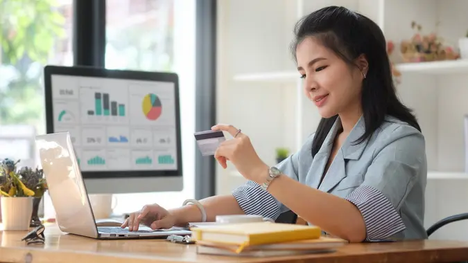 Happy young asian woman holding credit card and using computer for banking online. stock photo