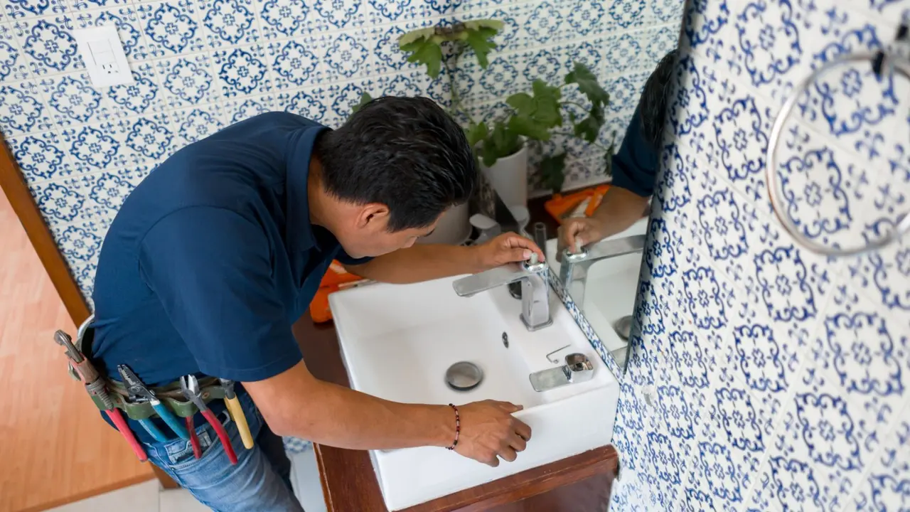 Latin American plumber installing a faucet in a bathroom's sink - home repairment concepts.