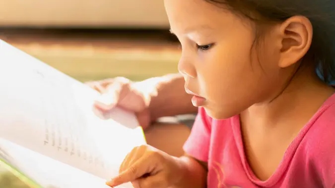 A young child pointing at words on a book, concentrating on learning how to read at home.