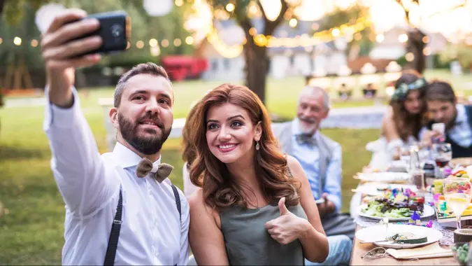 A couple taking selfie at the wedding reception outside in the backyard.