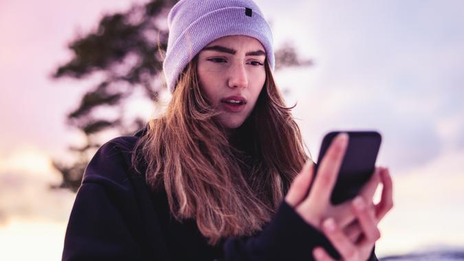 Teenage girl standing outdoors in the winter landscape checking the social media messages and emails on her smartphone.
