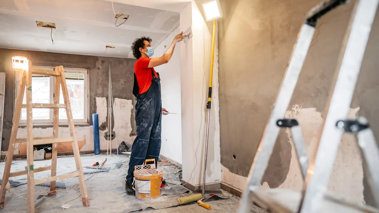A construction worker plastering and smoothing concrete wall in room.