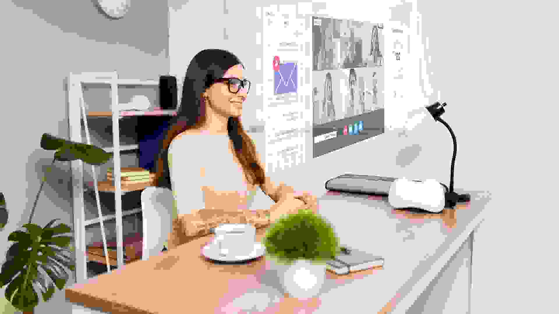 Cheerful latin woman working and smiling while using AR glasses at her office desk for an online video call.