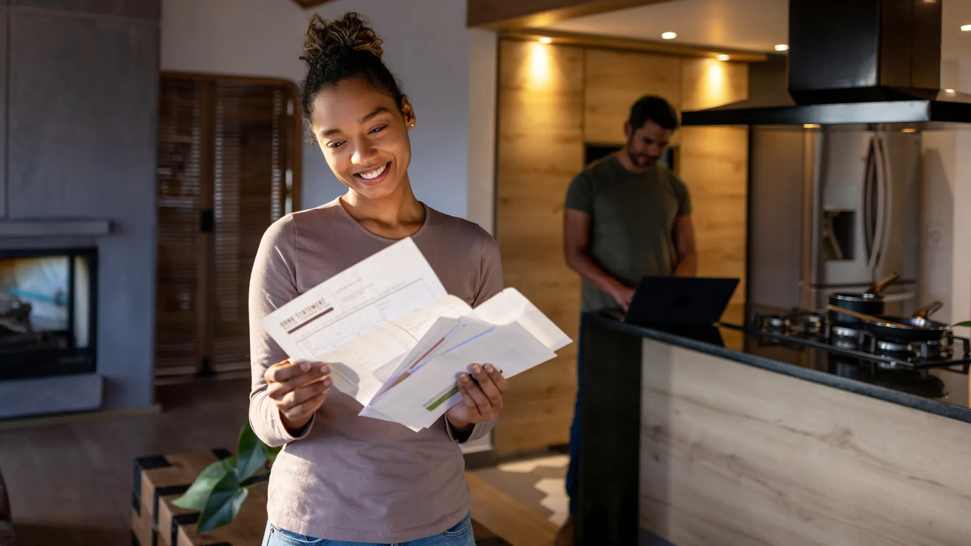 快乐的非裔美国妇女在家里看着邮寄来的水电费账单，微笑着。