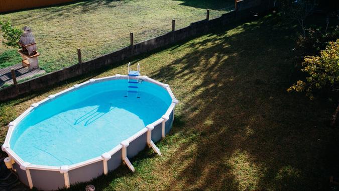 An above ground pool sets on grass in the backyard on a sunny summer day aerial view.