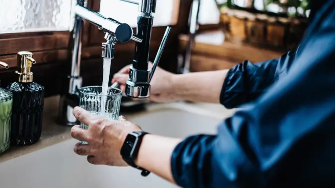 Close up of senior man in sportswear filling a glass of filtered water right from the tap after exercising at home. Staying hydrated while taking a break from daily training stock photo