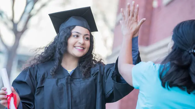 Female graduate high fives mother in celebration after graduation ceremony stock photo