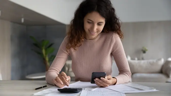 Smiling woman using smartphone and calculator, working with financial documents stock photo