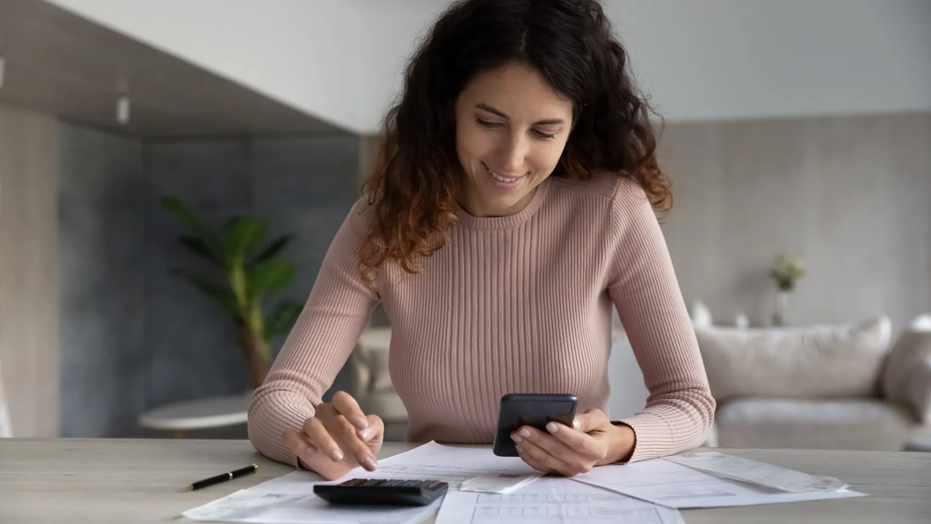 Smiling woman using smartphone and calculator, working with financial documents stock photo