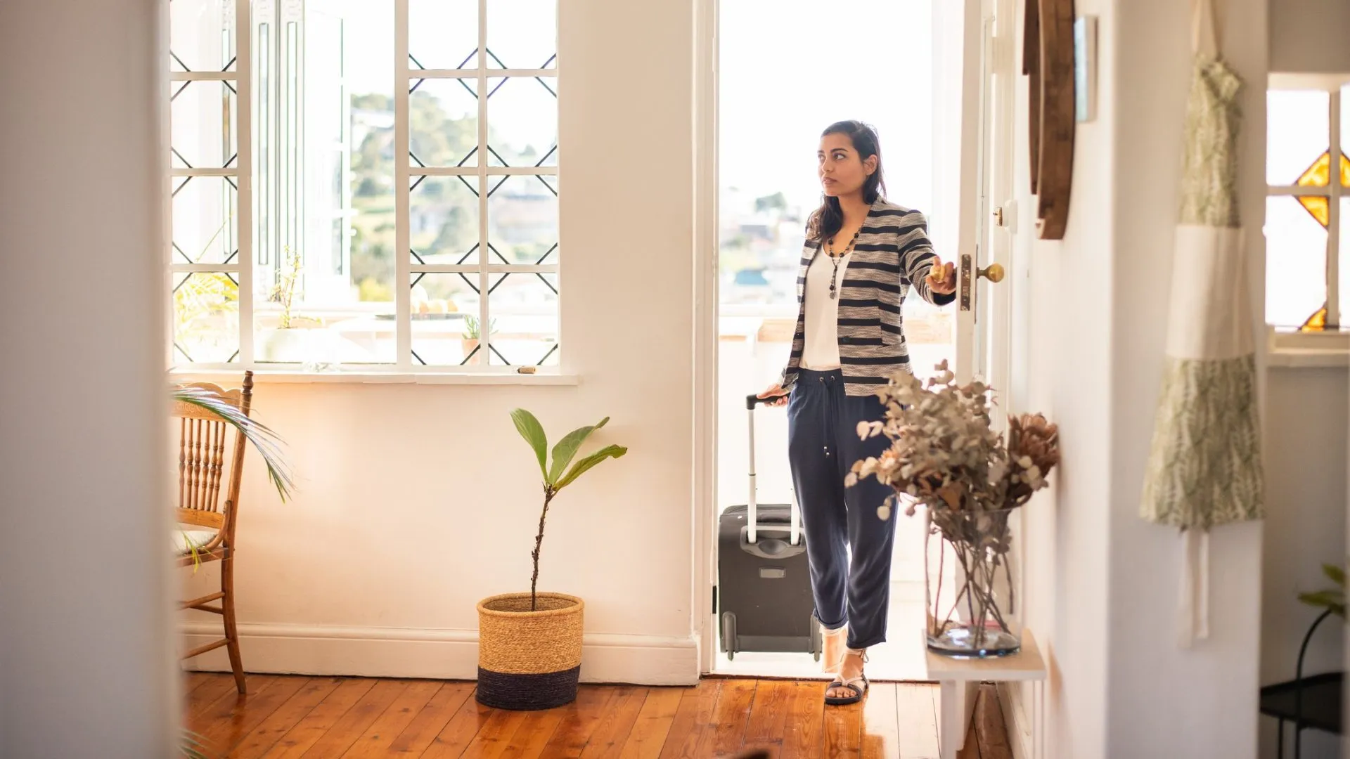 Young woman pulling a suitcase opening the front door of her rental accommodation during a vacation trip.