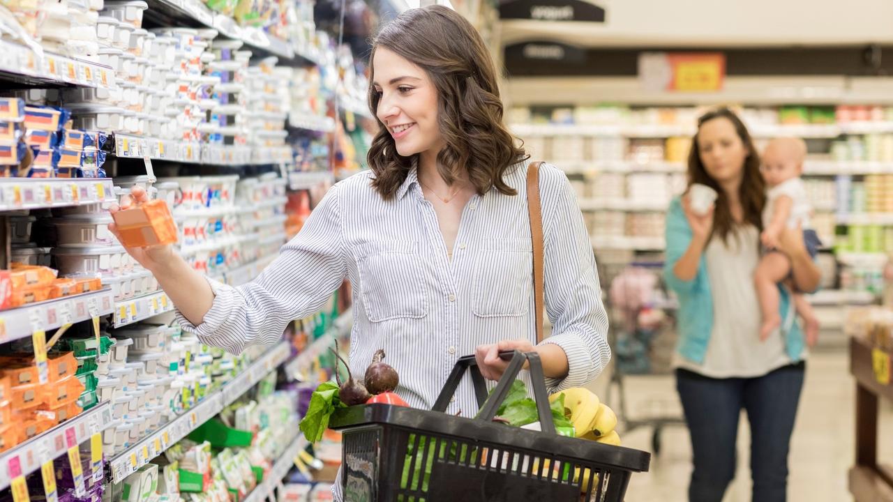 Young woman reads nutrition on a package of cheese in grocery store stock photo