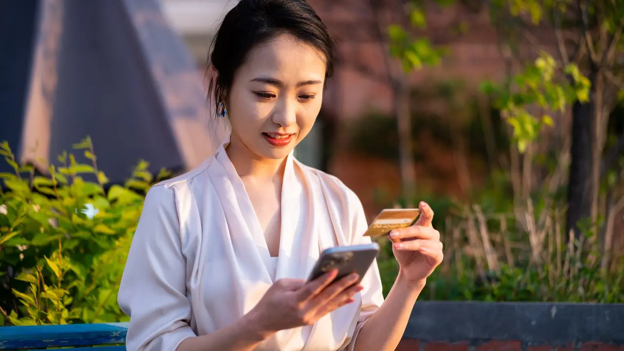 Asian young woman sitting on chair, paying with smart phone in city public park stock photo