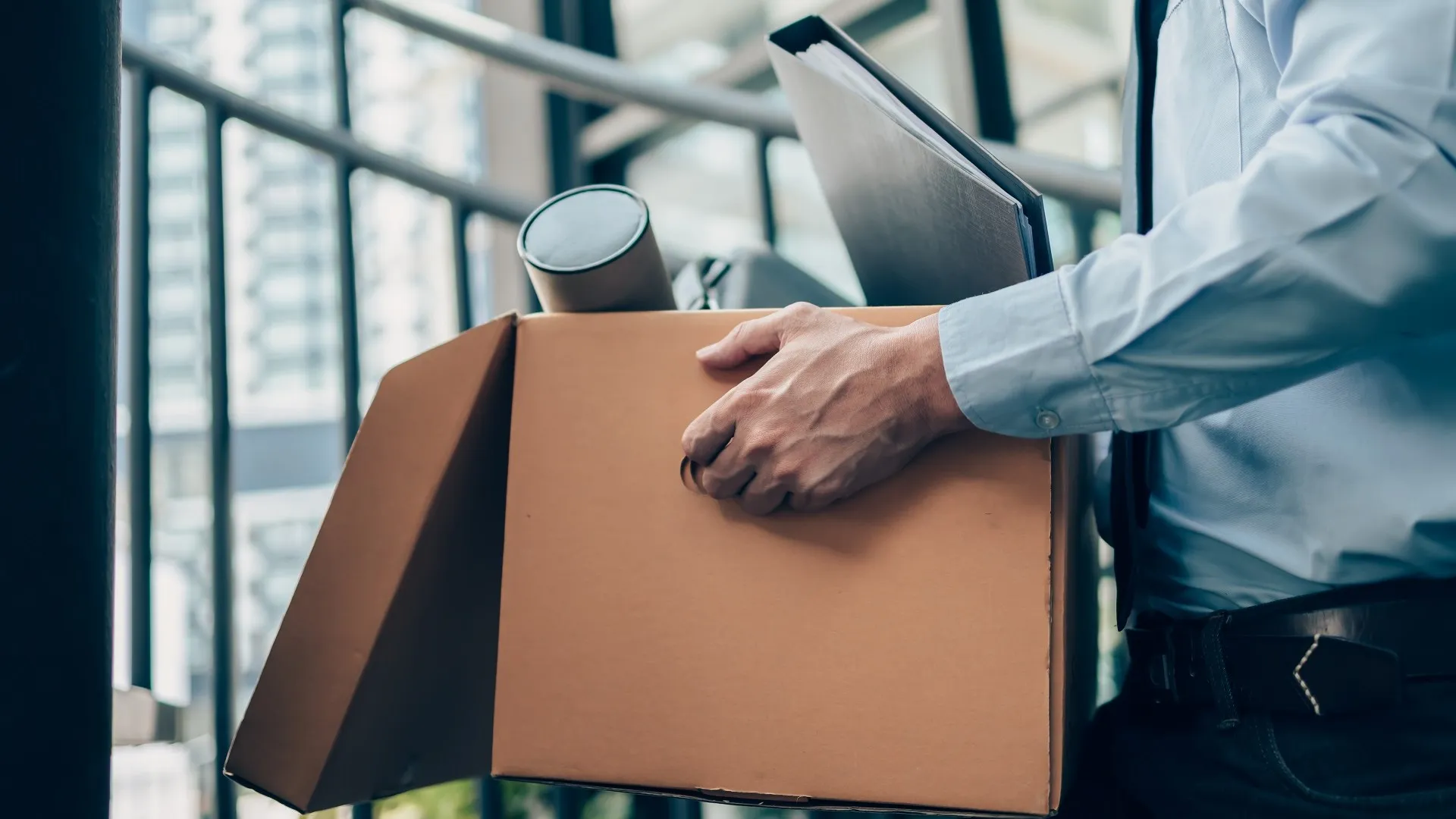 Unemployed hold cardboard box and laptop bag, dossier and drawing tube in box. Quitting a job, businessman fired or leave a job concept. stock photo