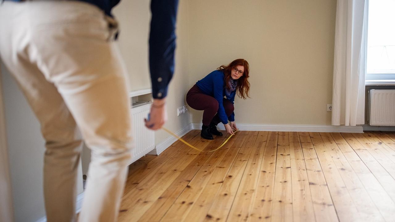 Woman crouching while measuring floor of new house with man stock photo