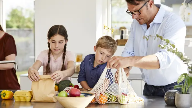 Man unpacking groceries with children in kitchen stock photo