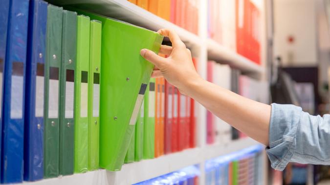 Male hand choosing new green ring binder file folder from colorful shelf display in stationery shop.