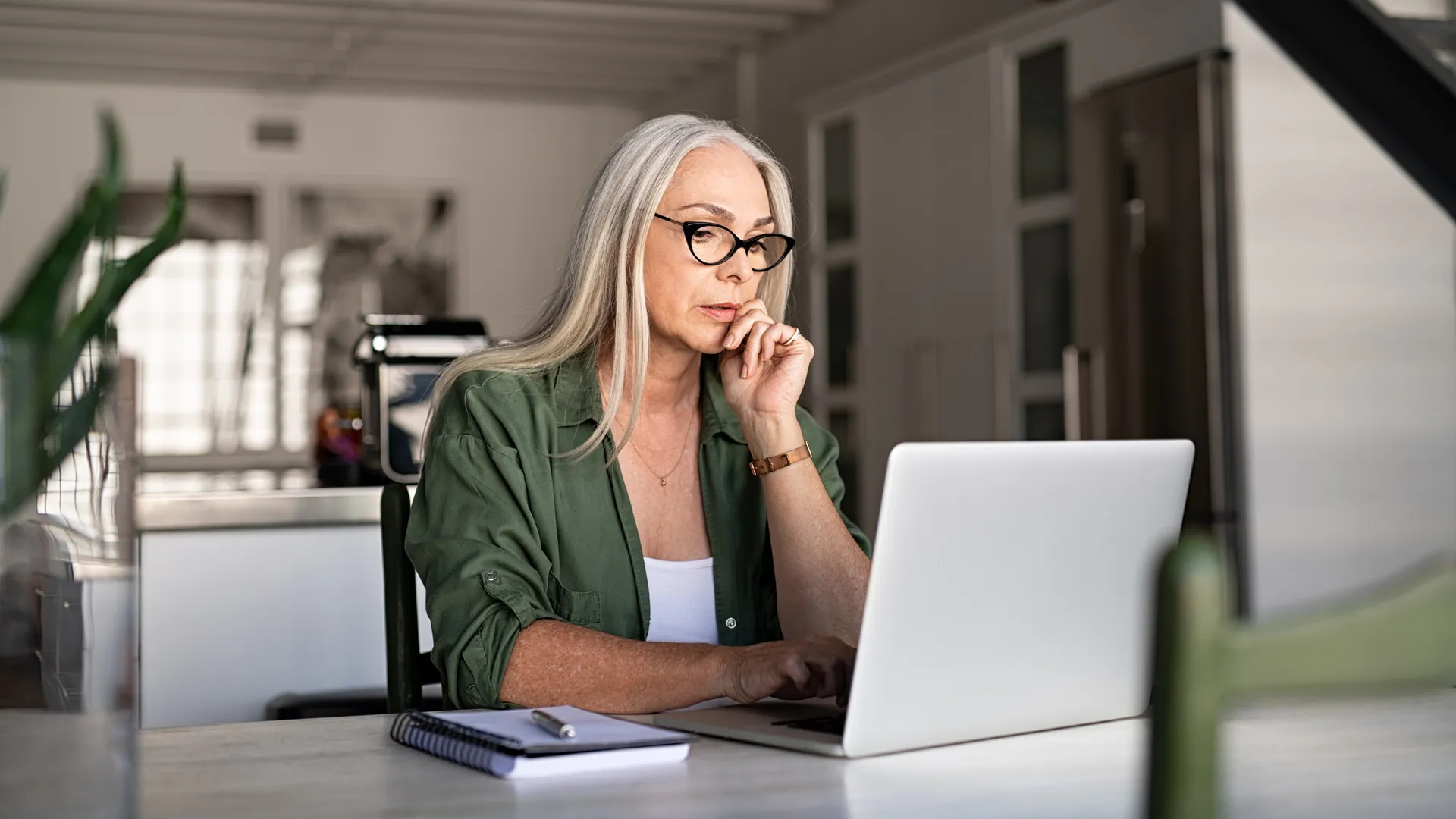 Focused old woman with white hair at home using laptop.