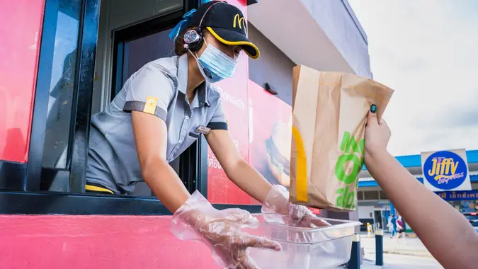 Bangkok, Thailand- April, 03, 2021 : Female staff at McDonald's deliver food to customers through the door of the car at the pick up point in Bangkok, Thailand.