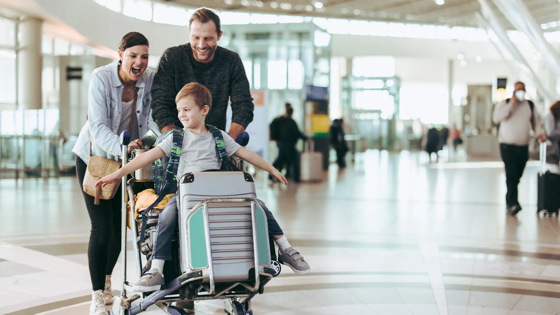 Couple happily pushing the trolley with their son at airport.