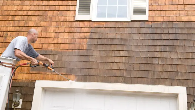Man in a bucket truck power washing exterior shingles.