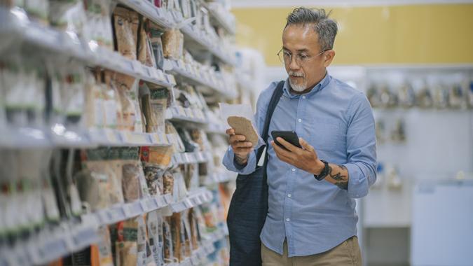 Asian chinese senior man checking shopping list using smart phone shopping in supermarket looking for dairy product stock photo