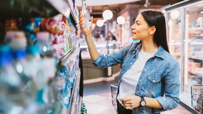 Happy young woman shopping in supermarket chooses water stock photo